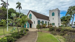 Une église dotée d’un clocher central, d’une galerie couverte et entourée de verdure.
