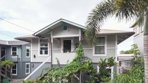 A two-story residential building with a balcony, a staircase, and a garden with various plants. - Charming 2BR Condo in Historic Wailuku | Central Maui Location (Wailuku)