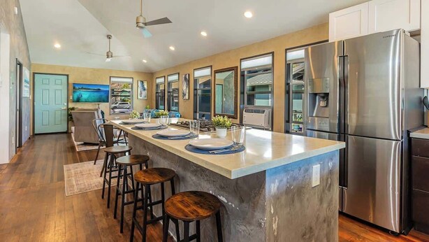 A modern kitchen with a central island, stainless steel appliances, and a dining area with bar stools. - Charming 2BR Condo in Historic Wailuku | Central Maui Location (Wailuku)