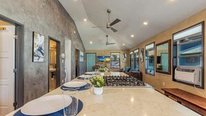A modern kitchen with a central island, a ceiling fan, and large windows. - Charming 2BR Condo in Historic Wailuku | Central Maui Location (Wailuku)