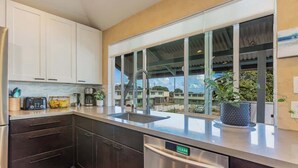 A modern kitchen with stainless steel appliances, a dishwasher, and a large window with a view of buildings. - Charming 2BR Condo in Historic Wailuku | Central Maui Location (Wailuku)
