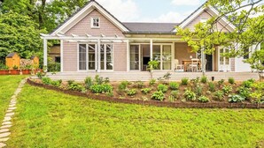 Une maison à deux étages dotée d’un porche abrité, d’un jardin avec différentes espèces de plantes et d’un chemin de pierre menant à l’entrée.