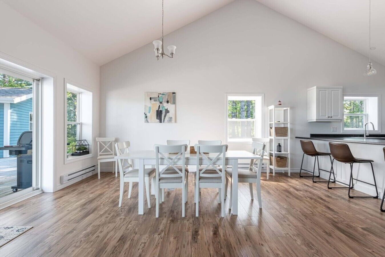 A spacious kitchen with white cabinetry, a dining area with white chairs, and a large window providing natural light.