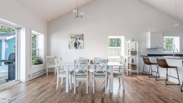 A spacious kitchen with white cabinetry, a dining area with white chairs, and a large window providing natural light.