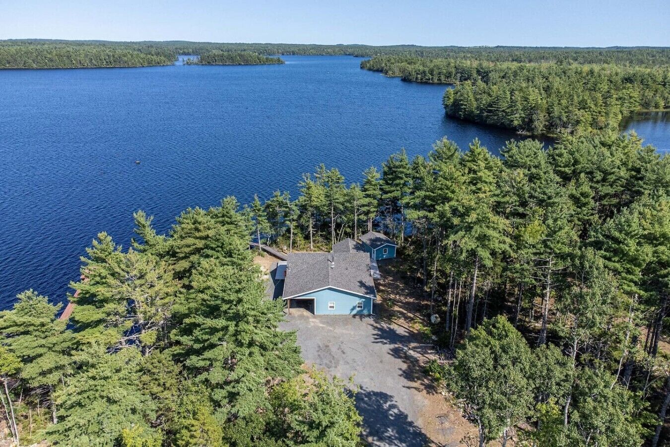 A house surrounded by dense forest and a large body of water.