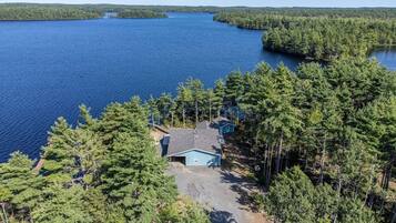 A house surrounded by dense forest and a large body of water.
