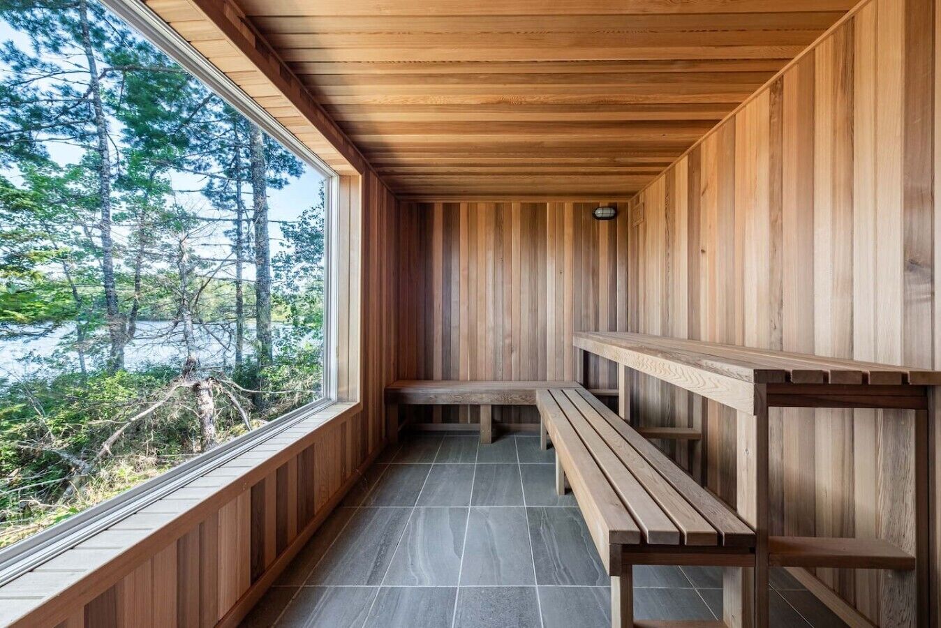 A wooden interior with benches and a large window overlooking a forested area.
