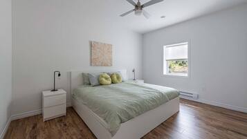 A bedroom with a bed, nightstands, a ceiling fan, a window, and a wall-mounted artwork.
