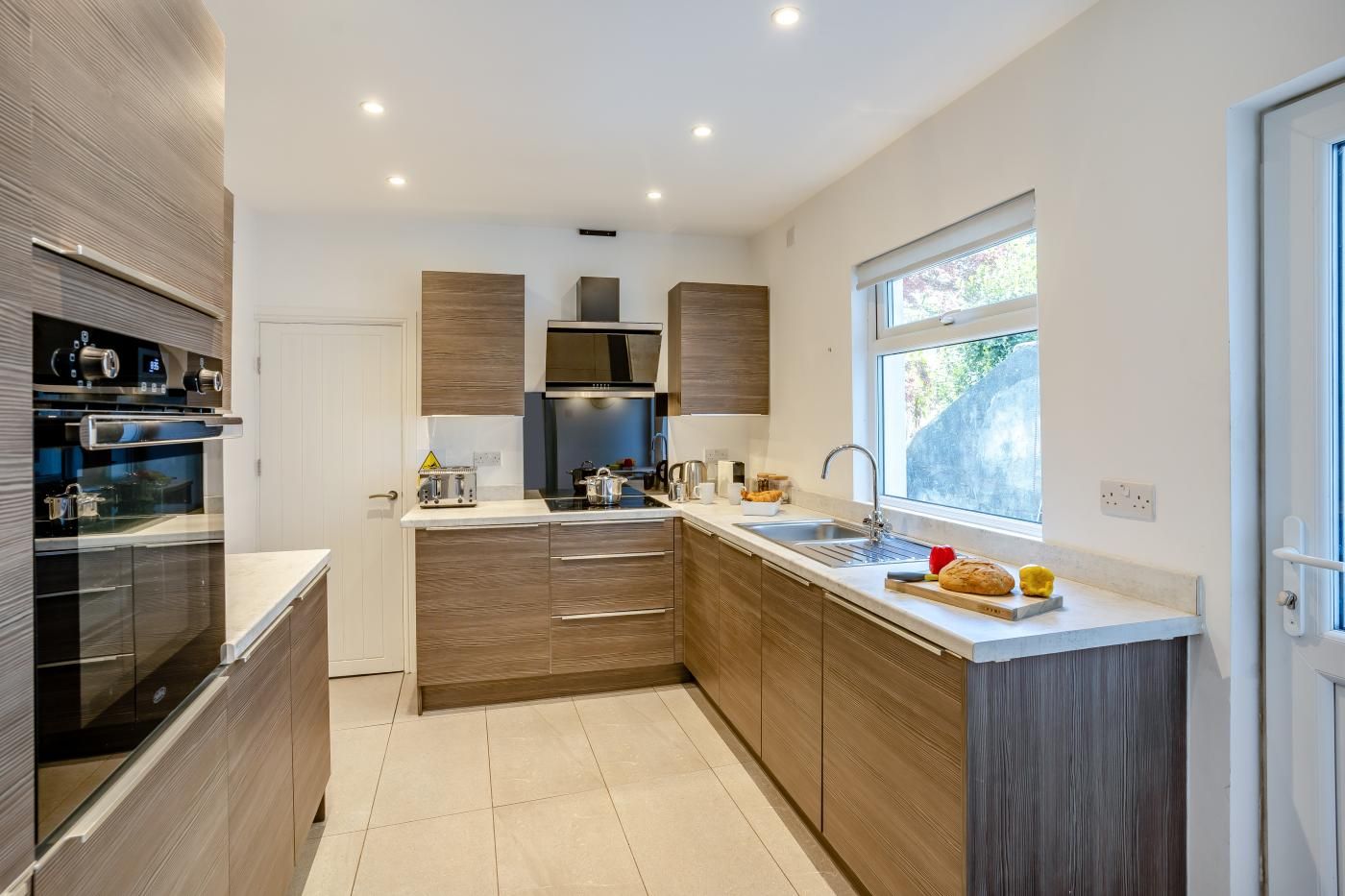 A modern kitchen with a built-in oven, a stainless steel range hood, and a window providing natural light.