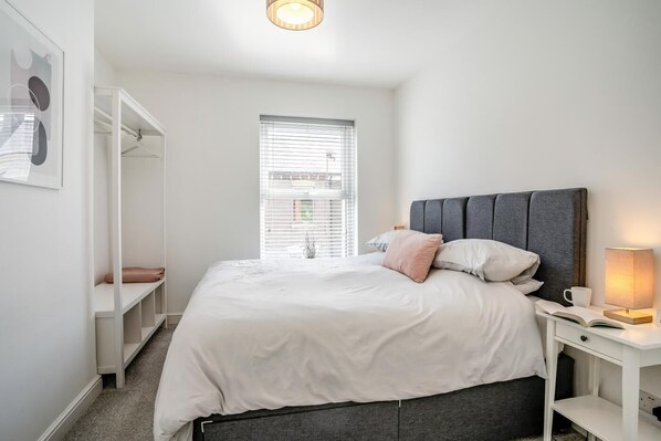 A bedroom with a bed, bedside table, and a window with blinds.