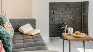 Ein modernes Wohnzimmer mit einem grauen Sofa, einem Couchtisch mit Gebäck, einer Wand aus schwarzen Ziegeln und einem weißen Vogelkäfig.