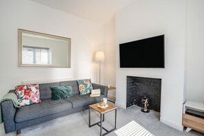 A modern living room with a grey sofa, a fireplace, a flat-screen TV, and a mirror on the wall.