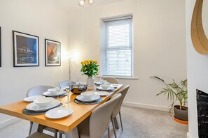 A dining area with a wooden table set for four, chairs, a vase with yellow flowers, and framed pictures on the wall. - 3 Bed in Cardiff (oc-bow188) (Cardiff)