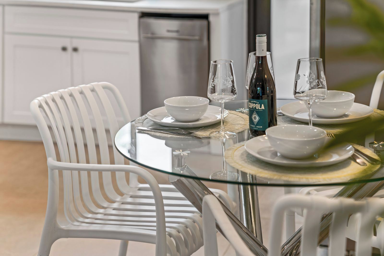 A dining table set with white plates, bowls, and wine glasses, with a bottle of Cuppola wine on the table.