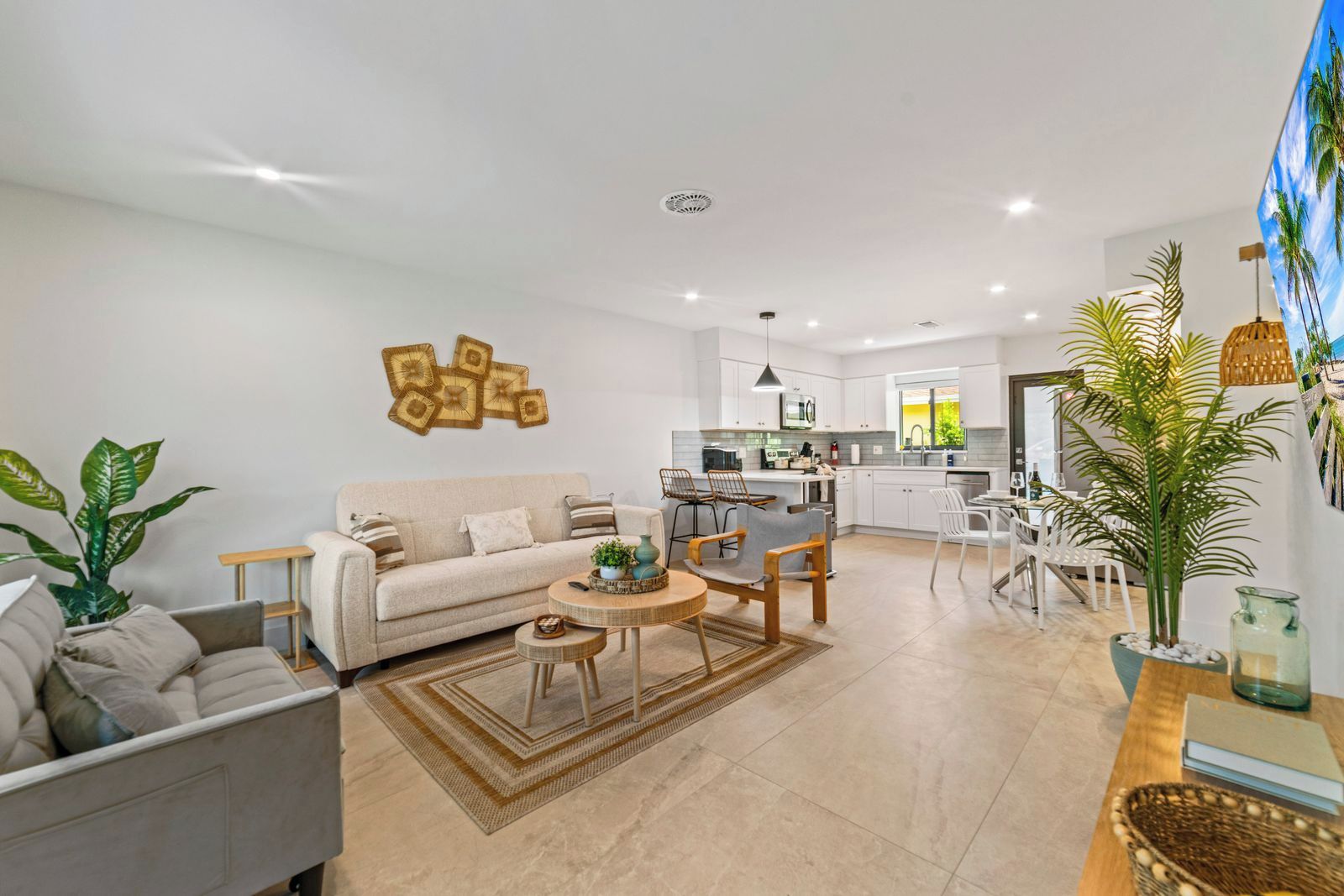 Un salon moderne avec un canapé, une table basse et des fauteuils, une cuisine avec des meubles blancs et un coin repas comprenant une table et des chaises.