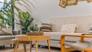 Ein Wohnzimmer mit einer Couch, einem runden Tisch und einem Sessel. Auf dem Tisch befinden sich eine Pflanze und eine Vase.