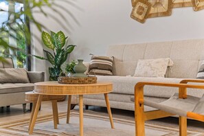 Ein Wohnzimmer mit einer Couch, einem runden Tisch und einem Sessel. Auf dem Tisch befinden sich eine Pflanze und eine Vase.