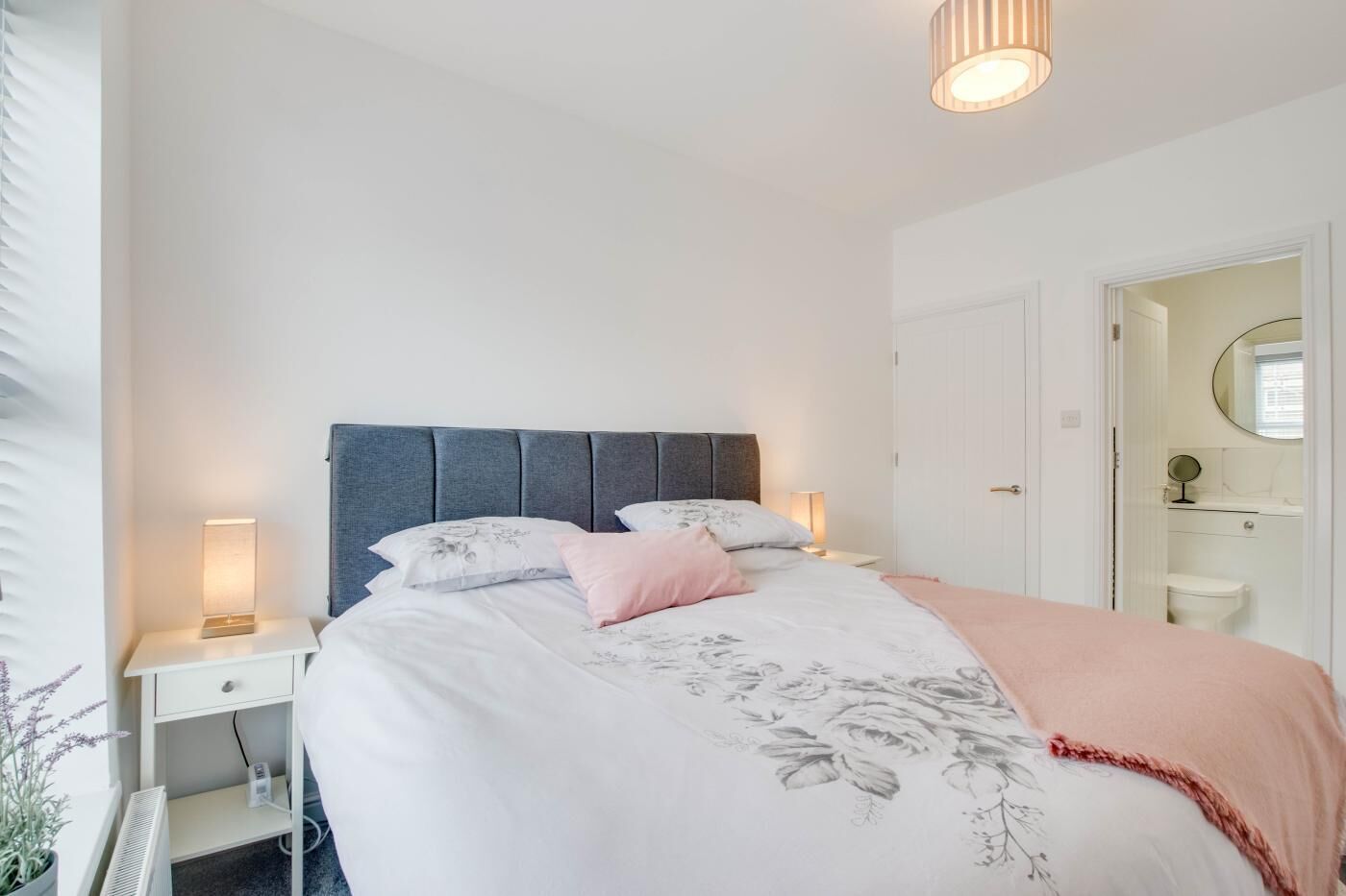 Une chambre à coucher comprenant un lit, des tables de chevet, une commode, une lampe, un miroir et une porte donnant sur une salle de bain.