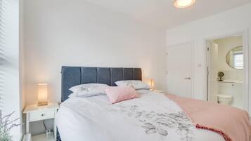 Une chambre à coucher comprenant un lit, des tables de chevet, une commode, une lampe, un miroir et une porte donnant sur une salle de bain.