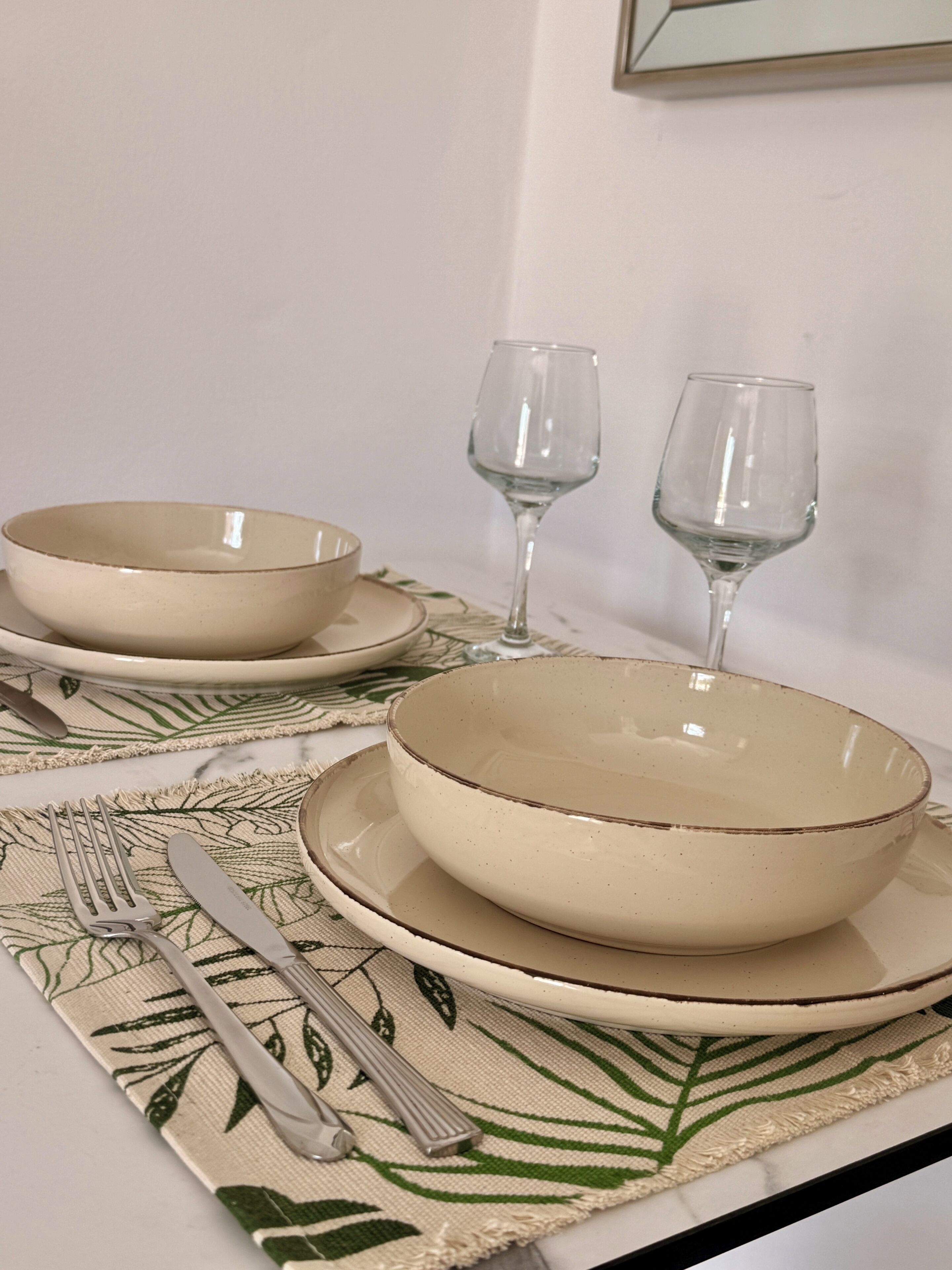 Una mesa servida con dos tazones, dos copas de vino, un tenedor y un cuchillo sobre un mantel individual.