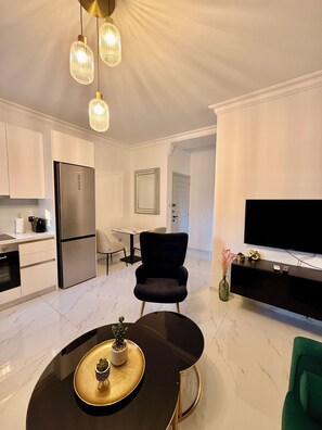 Eine moderne Küche mit Kühlschrank, Esstisch und Stühlen, ein Wohnbereich mit Fernseher und ein Essbereich mit Pflanze.