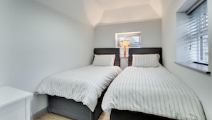 A bedroom with two beds, a window with blinds, a ceiling light, and a small window with a lamp. - 5 Bed in Bala (oc-bow163) (Bala)