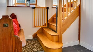 Una escalera de madera con barandilla, que lleva a un rellano con un banco de madera y una pequeña mesa.