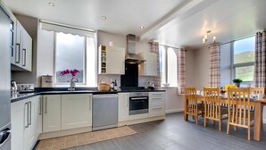 Una cocina moderna con armarios blancos, lavavajillas y un comedor con sillas y una mesa de madera.