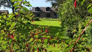 Un bâtiment en pierre doté d’un toit en pente, entouré d’une végétation luxuriante et d’une pelouse bien entretenue.