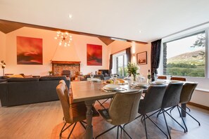 Uma área de jantar moderna com uma mesa grande para seis pessoas, lareira de pedra e vista para o exterior.