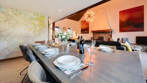 Un coin repas avec une longue table dressée pour six personnes, une cheminée en pierre et un grand tableau abstrait accroché au mur.