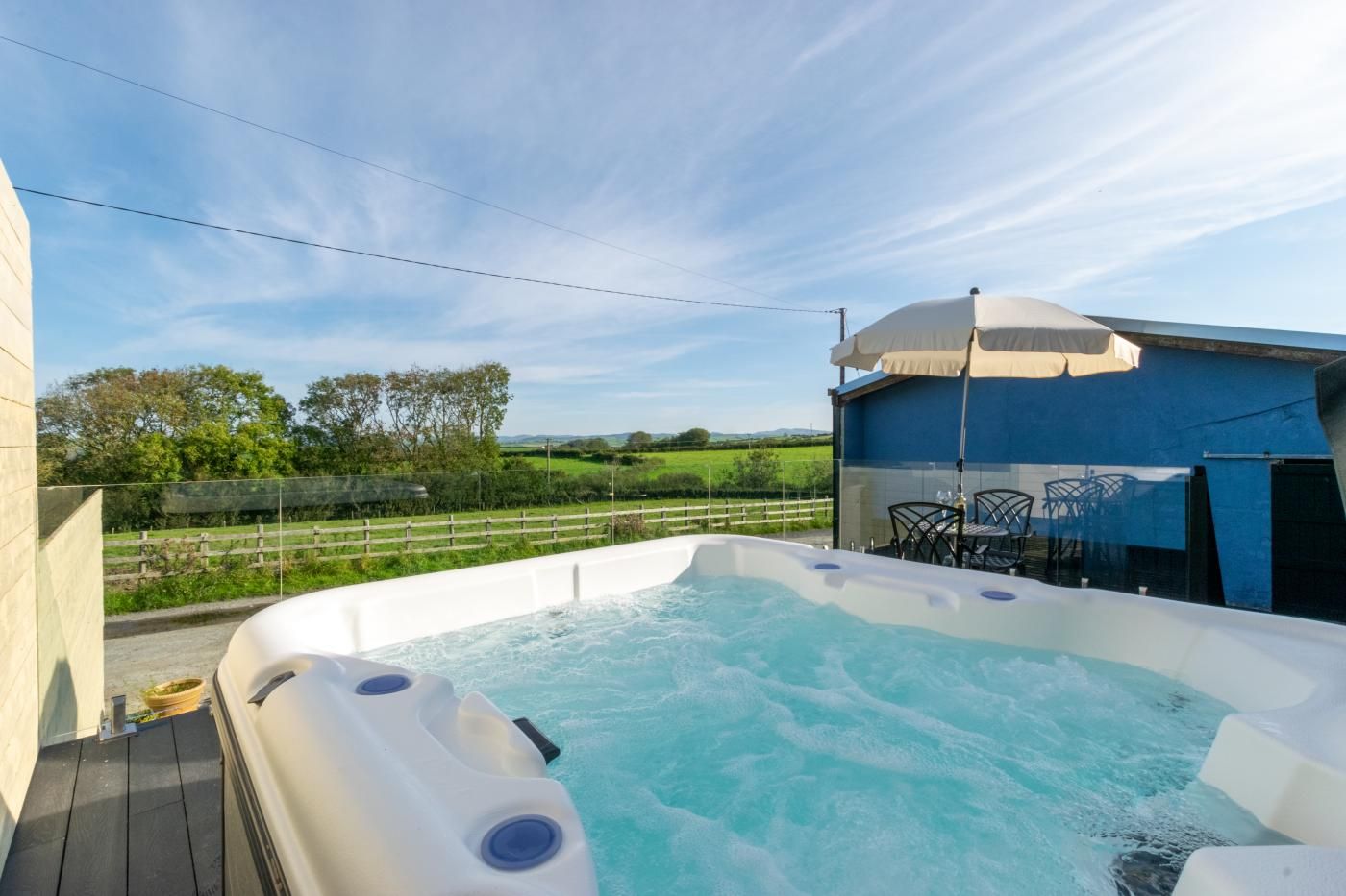 Een bubbelbad met uitzicht op een groen landschap, een terras en een overdekte zithoek.