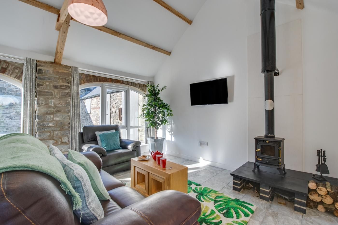 A living room with a stone wall, a fireplace, a sofa, a coffee table, and a TV mounted on the wall.