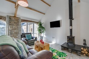 A living room with a stone wall, a fireplace, a sofa, a coffee table, and a TV mounted on the wall. - 1 Bed in Aberystwyth (oc-bow182) (Rhos-y-garth)