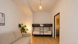 Una habitación con sofá, literas, lámpara colgante y una planta en maceta.