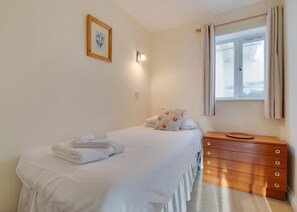 Una camera da letto con un letto, un comodino, una cassettiera, una finestra con tende e una lampada fissata al muro.