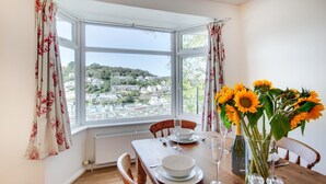Un coin repas avec une table dressée pour quatre personnes, une vue sur la ville par une grande baie vitrée et un vase rempli de tournesols.