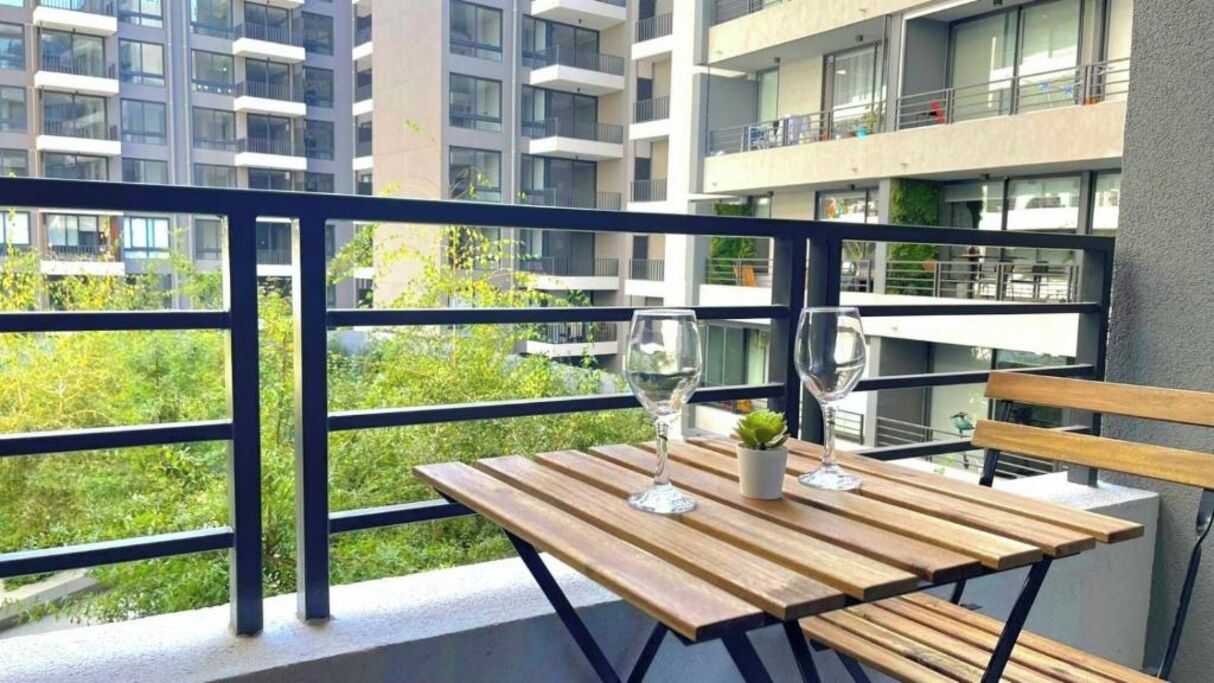 Un balcon avec une table en bois, deux verres à vin et une petite plante en pot.
