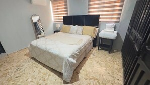 A bedroom with a bed, bedside tables, a chair, a mirror, and a wardrobe. - ARIAS PROPERTIES (Baní)