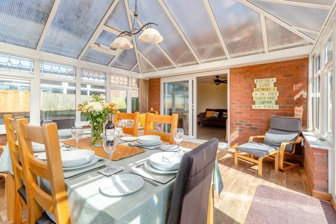 A conservatory with a dining area, a brick wall with a sign, and a view into the living room.