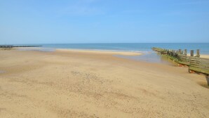 Een strand met een houten looppad dat naar het water leidt, een zandstrand en een heldere lucht.