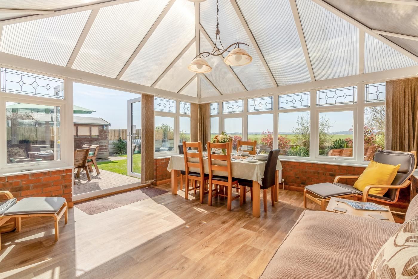 A conservatory with a dining table, chairs, and a seating area with cushions.
