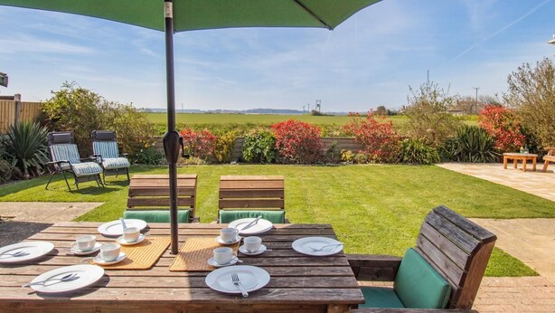 Een terras buiten met een eettafel, omringd door stoelen en een parasol.