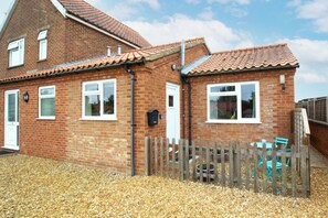 A two-story brick house with a tiled roof, a wooden fence, and a gravel driveway. - 1 Bed in Burnham Market (oc-2193) (Burnham Market)