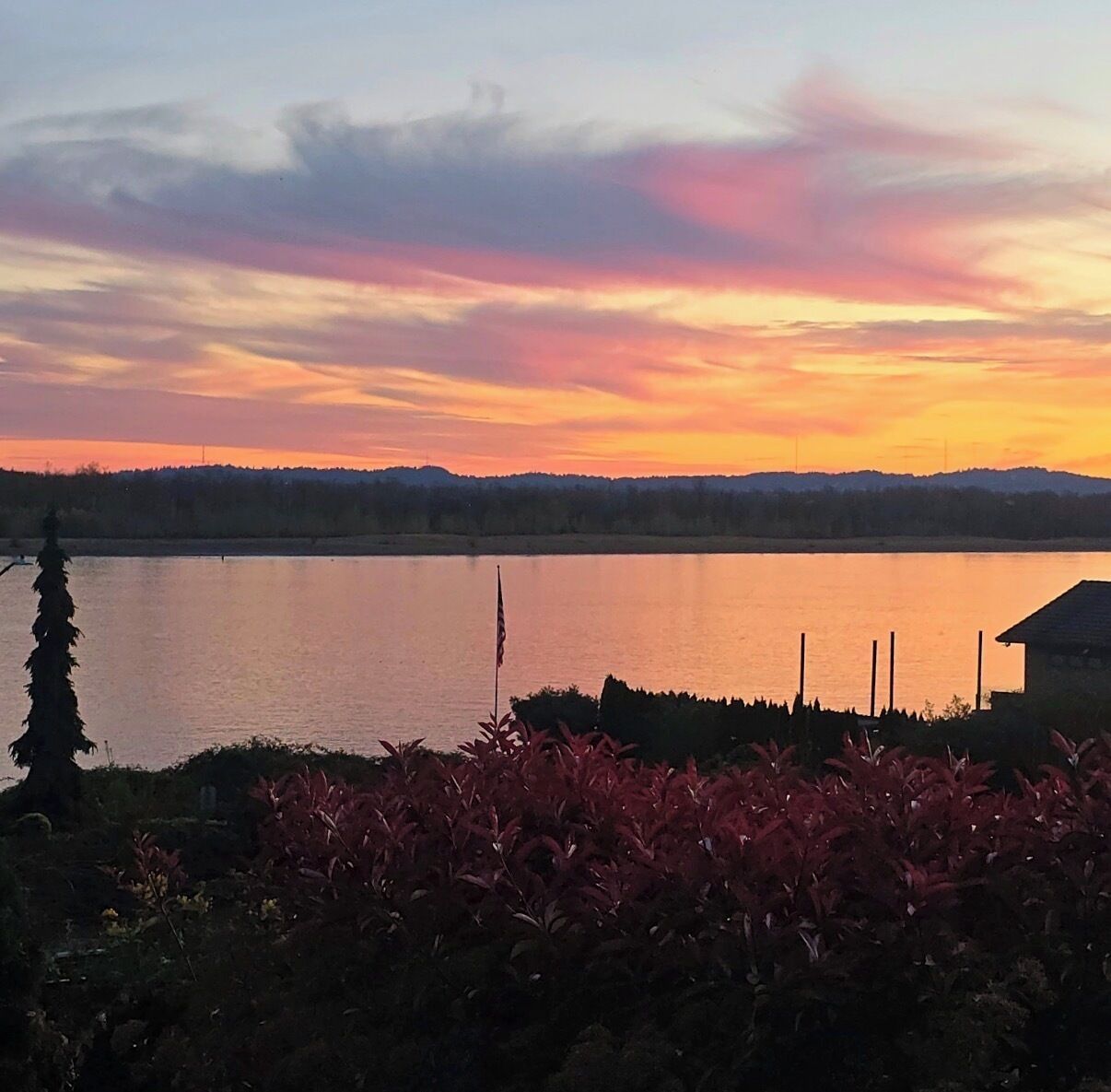 A serene lakeside view with a sunset, a flagpole, and a building in the foreground.