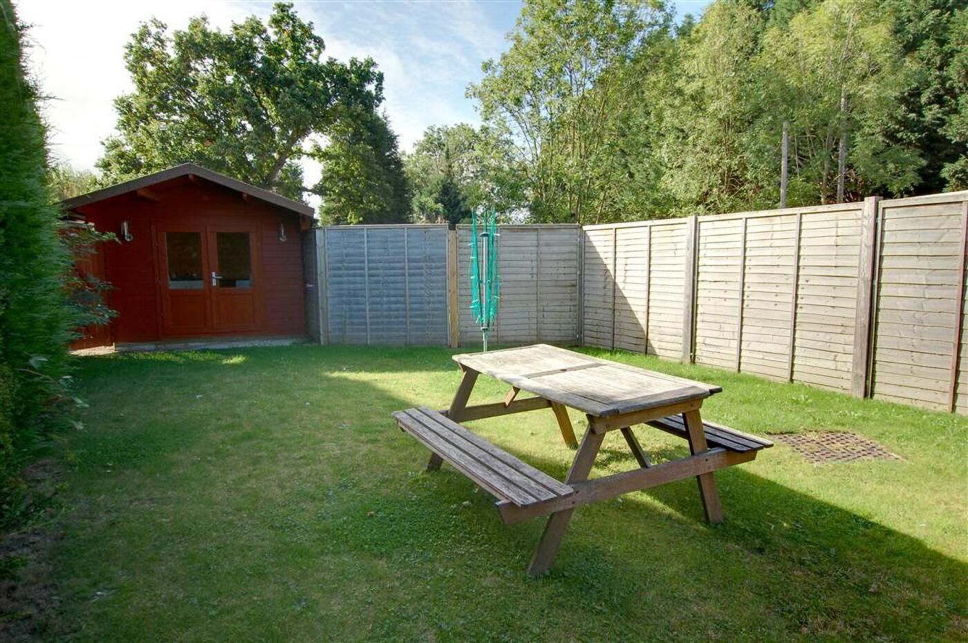 Un jardin avec une table de pique-nique en bois, un abri de jardin rouge et une clôture en bois.