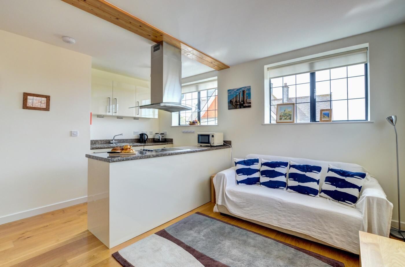 Ein kompakter Wohnraum mit einer Küchenzeile, einem Sofa mit gemusterten Kissen und Blick auf die Stadt durch große Fenster.