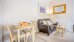 Un salon avec un canapé en cuir marron, une table à manger en bois avec des chaises, une petite table d’appoint, un tableau encadré au mur et un lampadaire.