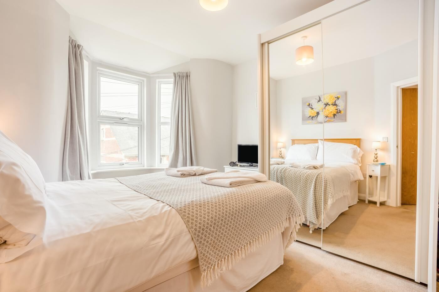A hotel room with a large bed, a smaller bed, a TV, a desk, and a mirror.
