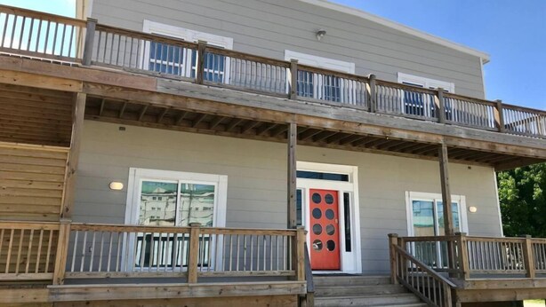 A two-story building with a balcony, a red door, and a wooden deck. - Whale of a Time offers a thoughtfully designed space (Galveston)